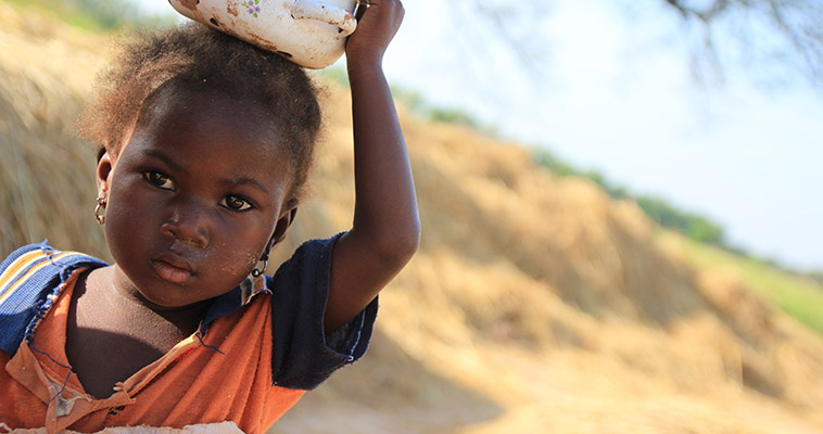 A little girl stands beside her family's harvested rice.