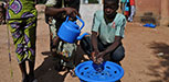 A man washes his hands over a blue bucket