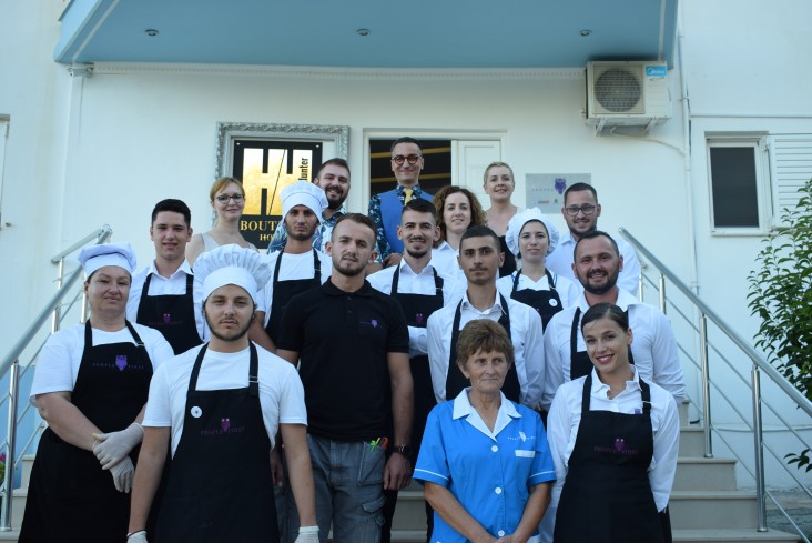 A group of staff who work at a hotel pose on stairs in front of hotel sign