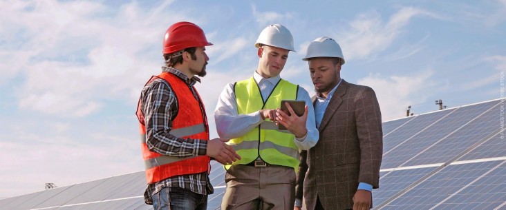 Three engineers examine data on a tablet in front of a large photovoltaic array