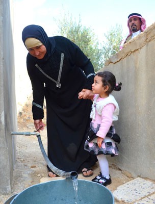 Al Khaldi looks on as his wife and granddaughter pump water from their storage tank.