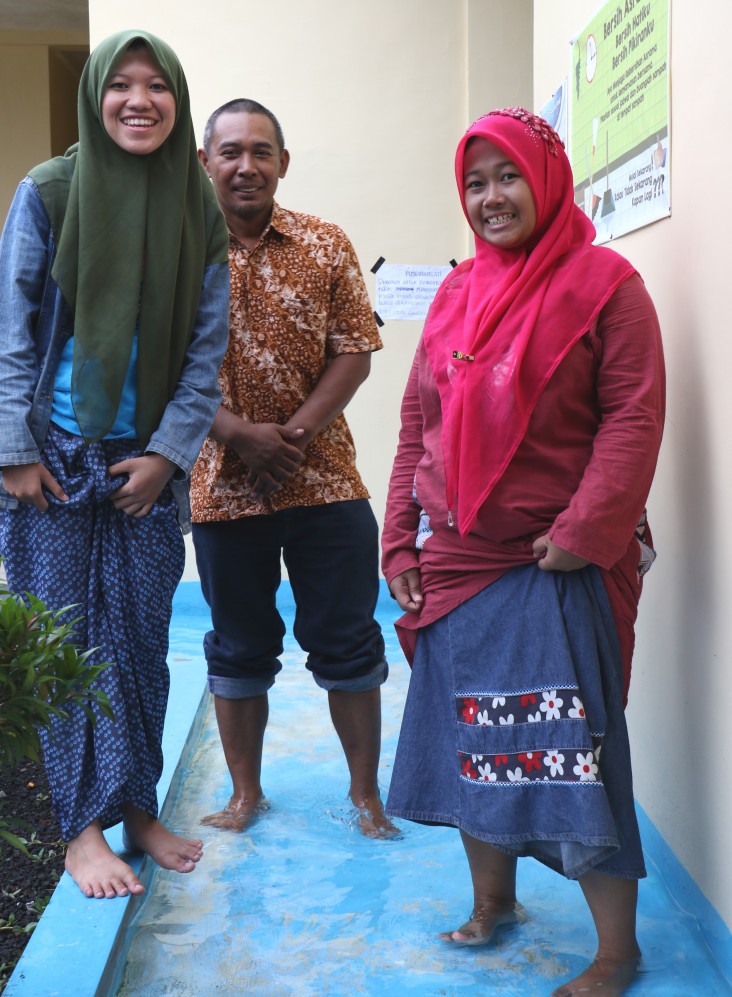 Female students and a school staff member demonstrate the foot-cleaning area at the sanitation facilities at the Ngalah Boarding School.