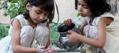 One little girl pours water over another little girls soapy hands.