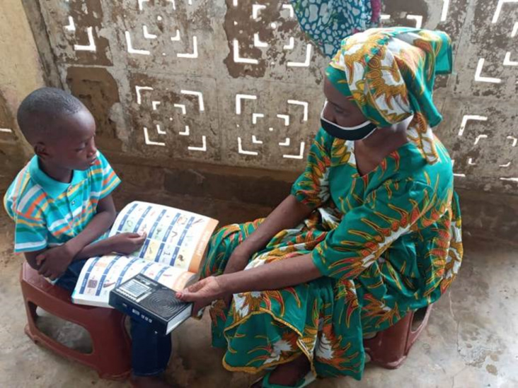 Mme Mariama Diallo aide son fils à étudier à la maison grâce aux programmes radiophoniques de Lecture Pour Tous et aux matériels de lecture à domicile. 