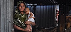 A mother holds her child in the doorway of their home.