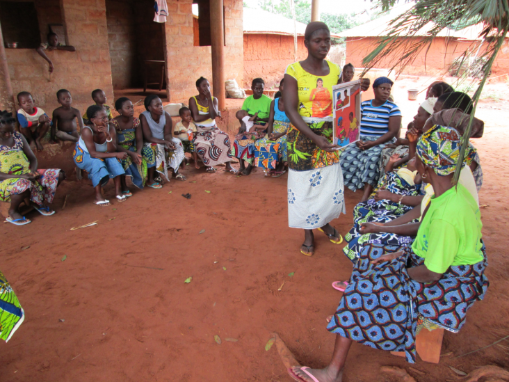 A facilitator leads a discussion with a women's group using the Tekponon Jikuagou story cards about couple communication, family