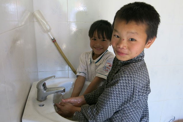 Two boys was their hands in a bathroom sink