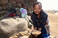 A young woman holding grain with a child in the background