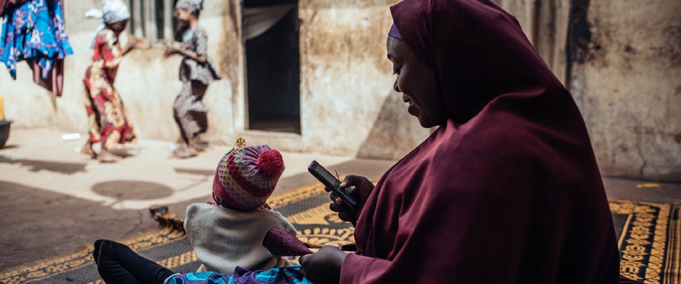 Woman in Nigeria sits on mat and uses mobile phone for digital health. Photo credit: KC Nwakalor, USAID