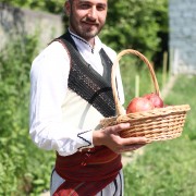 A young man dressed in traditional clothes holds a basket of pomegranites