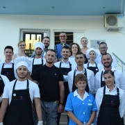 A group of staff who work at a hotel pose on stairs in front of hotel sign