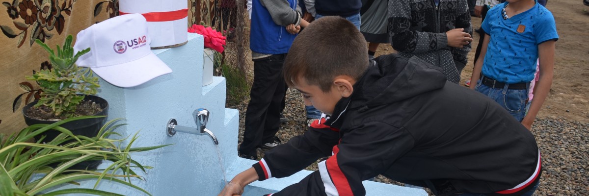 A boy washes his hands at a public fountain